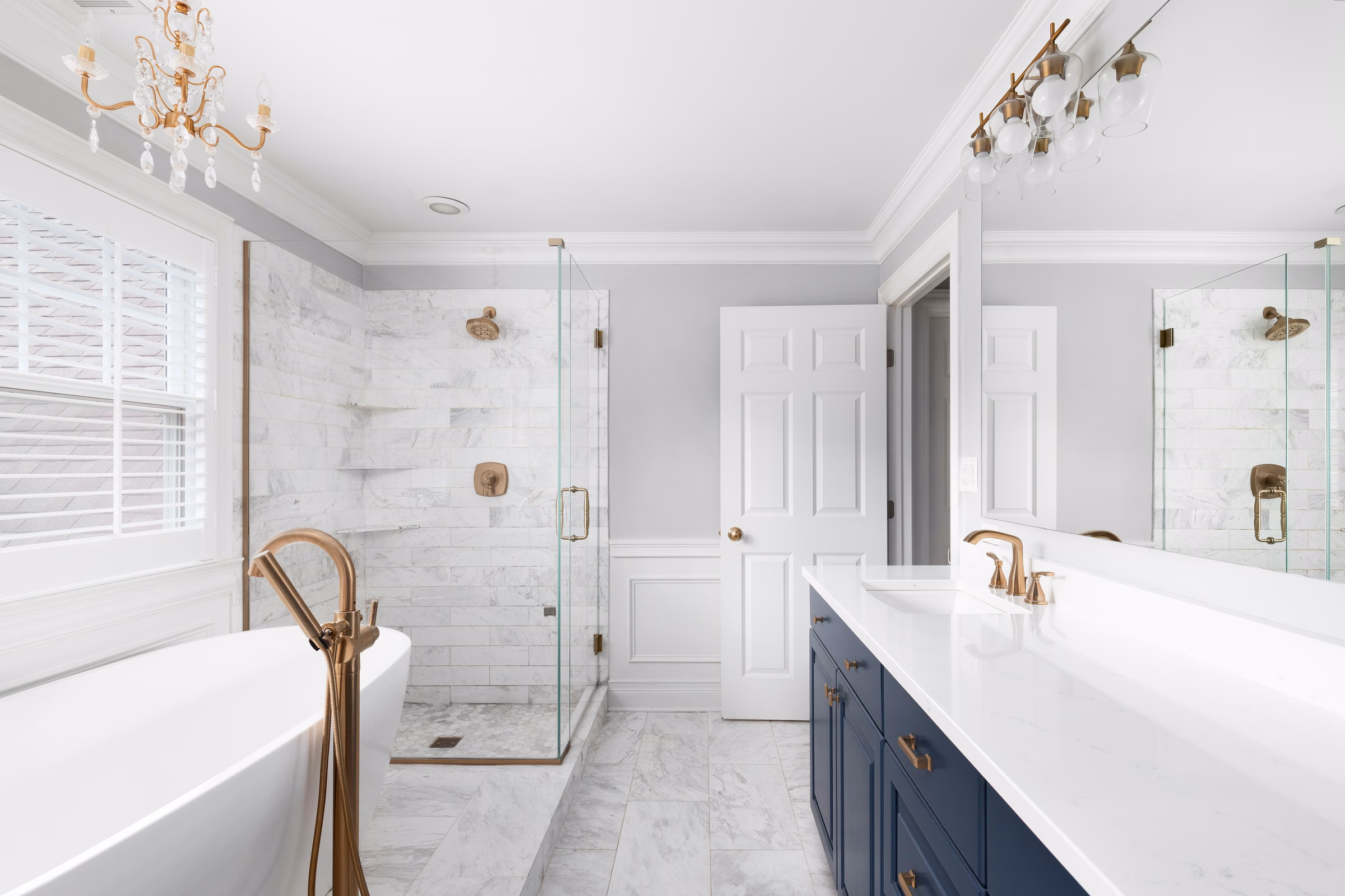 Newly renovated coastal bathroom with a navy vanity, freestanding tub, glass shower, and brass fixtures